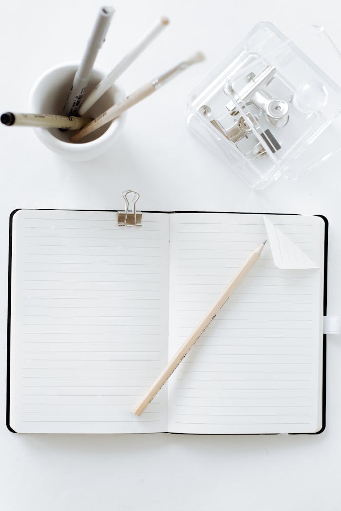 our-story-01 Top view of an open notebook with pen, pencils, and stationery items on a white surface.